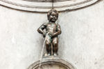 a statue of a boy with water coming out of it with Manneken Pis in the background