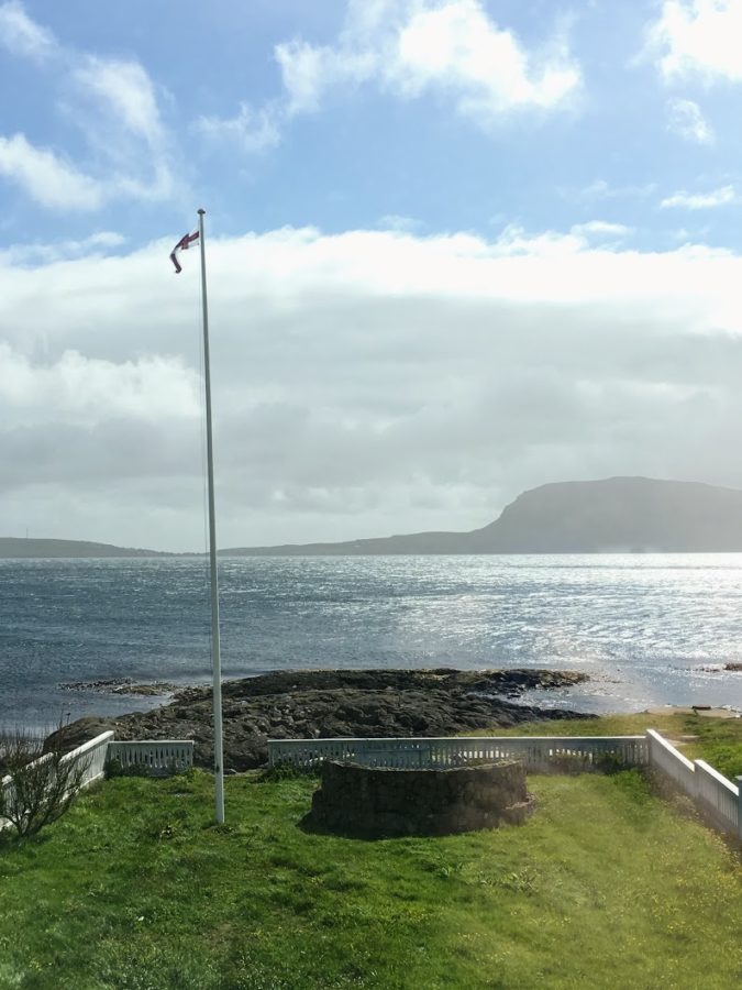 a flag pole on a grassy area by a body of water