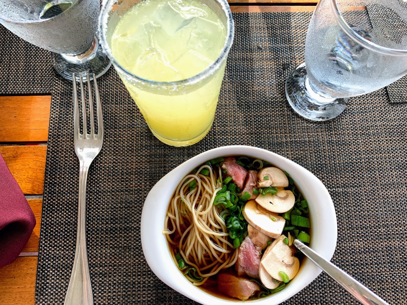 a bowl of soup with noodles and vegetables next to a glass of water