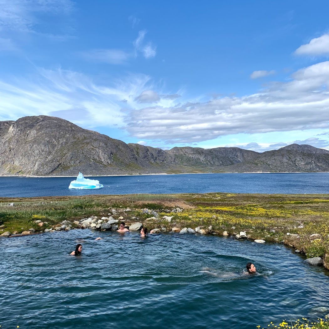 a group of people in a pool of water with a large iceberg in the background