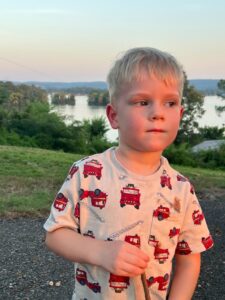 a boy standing outside with a body of water in the background